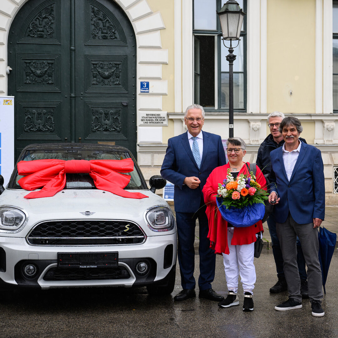 Innenminister Joachim Herrmann mit Gewinnern neben BMW Mini mit Schleife