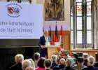 Herrmann im historischen Saal am Rednerpult, im Hintergrund Leinwand mit 25 Jahre Sicherheitspakt für die Stadt Nürnberg