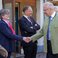 Innenminister Joachim Herrmann schüttelt einer Frau die Hand, weitere Personen am Eingang