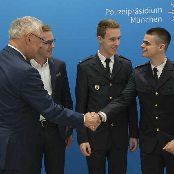 Auf dem Bild ist Innenminister Joachim Herrmann mit jungen Polizisten zu sehen, einem davon schüttelt er lächelnd die Hand.